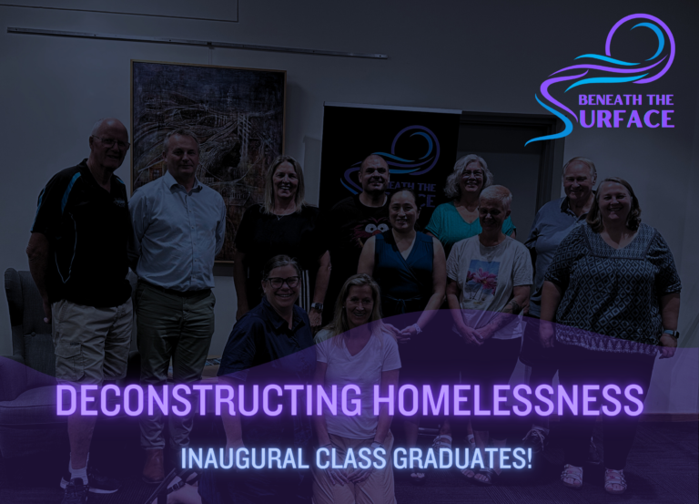 Article title card over a photograph of about a dozen people standing together indoors. Text reads: Deconstructing Homelessness — Inaugural Class Graduates.