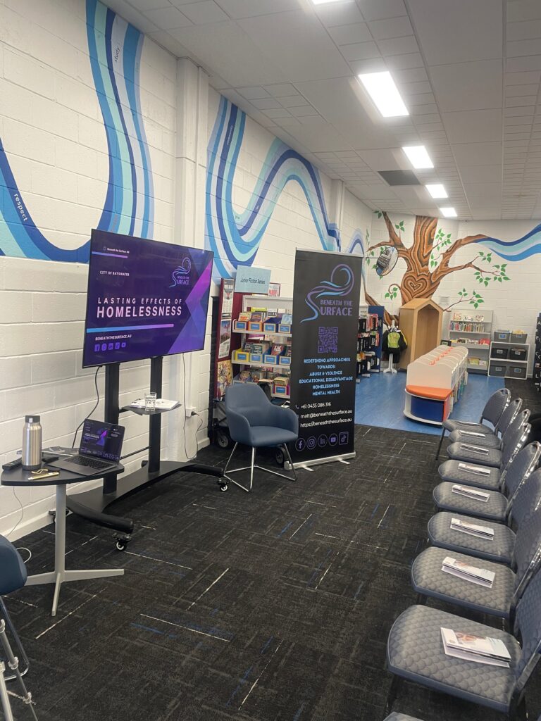 A library presentation space set up with a screen showing the City of Bayswater 'Lasting Effects of Homelessness' slide, a Beneath the Surface pull-up banner, and rows of empty chairs.